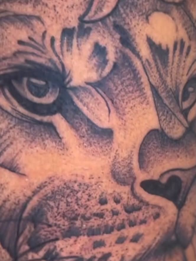 Close-up of a black and grey lion face tattoo with detailed eye and fur shading.