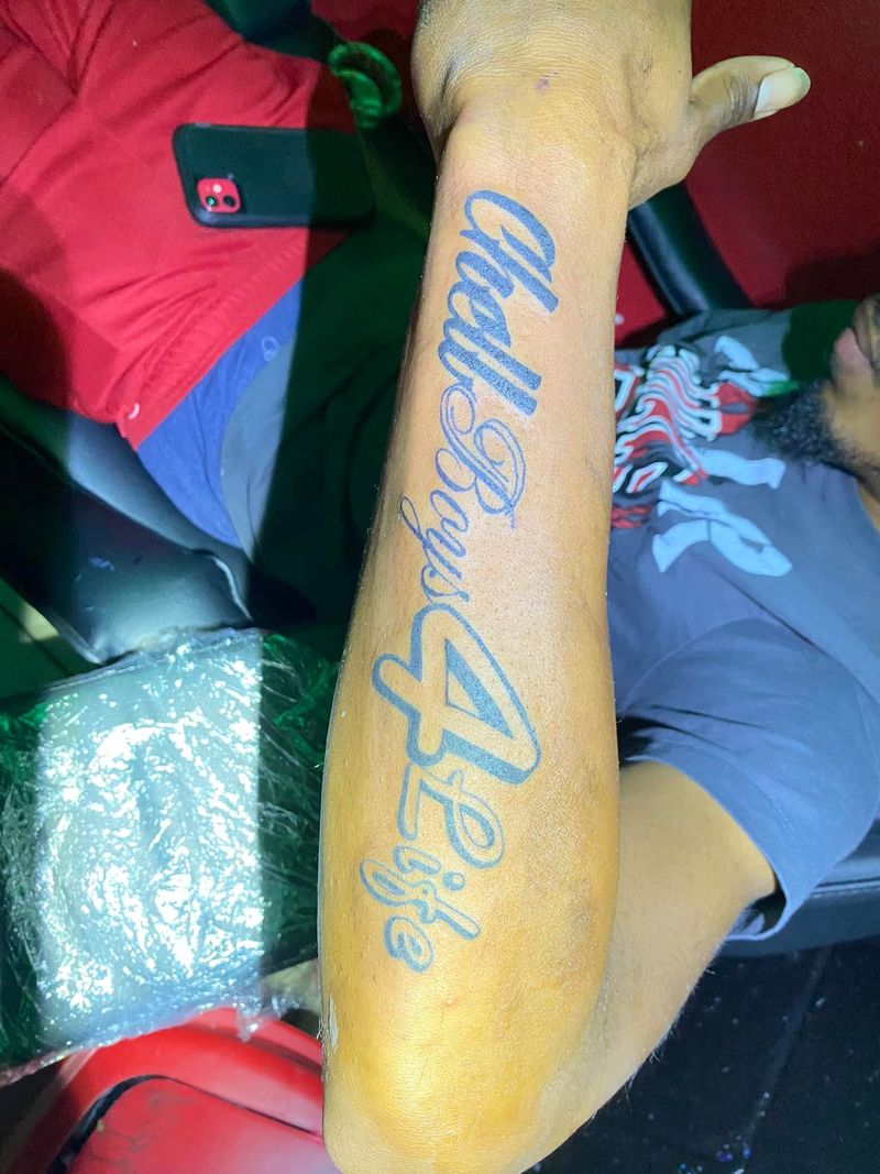 Blue script lettering tattoo running the length of a forearm.